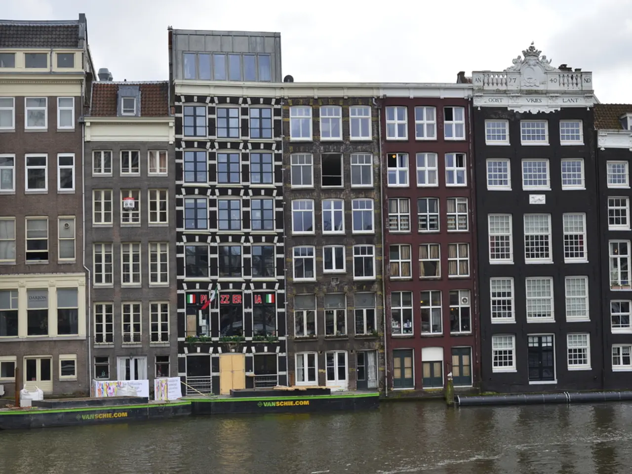 In this image we can see buildings, windows, there is an air conditioner, there are some posters,...