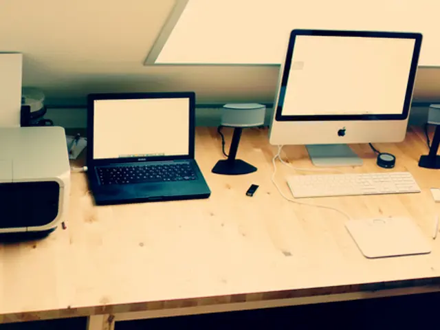 In this image we can see printer, laptop, speakers, monitor, keyboard and some things on table.