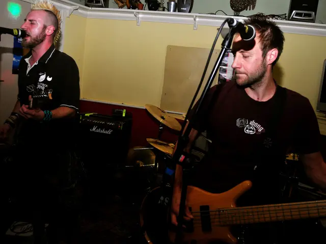 In this picture there are two members standing and playing guitars in their hands. One of the guy...