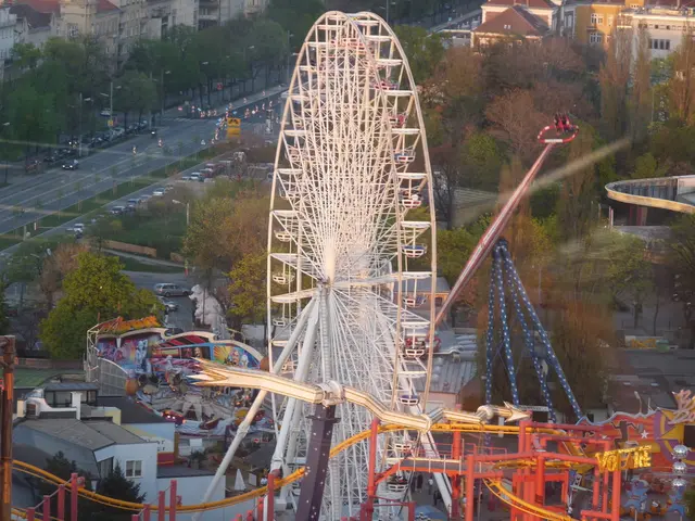 In this image there is a giant wheel. There are vehicles on the road. There are street lights on...