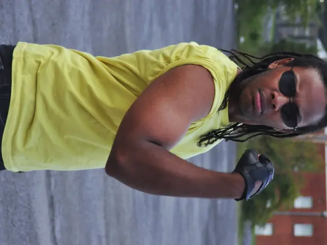 In this picture I can see a man wore sunglasses and I can see a building and few trees.