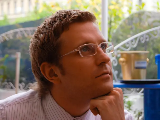 In the image there is a man with spectacles. Behind him on the right side of the image there is a...